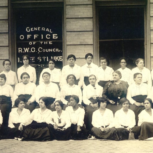 3 rows of professional black women pose outside of a storefront